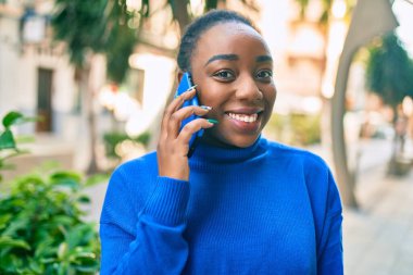 Genç Afrikalı Amerikalı kadın gülümsüyor. Şehirdeki akıllı telefondan mutlu bir şekilde konuşuyor..