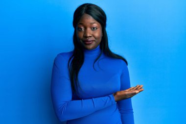 Avuç içi açık bir şekilde öne çıkan Afrikalı genç bir kadın yüzünde ciddi bir ifadeyle rahatlamış. Basit ve doğal bir şekilde kameraya bakıyorsun.. 