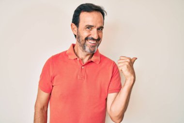 Orta yaşlı İspanyol bir adam, günlük kıyafetler giyiyor, gülümsüyor, gülümsüyor ve başparmağıyla yan tarafa bakıyor.. 