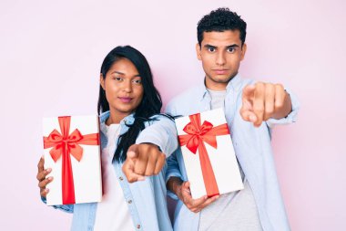 Güzel, genç bir çift yıldönümü kutlaması için hediyelerini tutarken kamerayı ve seni işaret ediyorlar. Kendine güvenen bir jest ciddi görünüyor. 