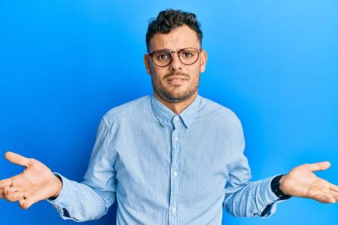 Gündelik kıyafetler giyen ve gözlüklü genç bir İspanyol. Kolları açık ve kafası karışık. Fikri bile yok.. 