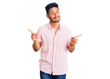 Gündelik tişört giyen yakışıklı Latin Amerikalı genç adam parmaklarıyla farklı yönleri işaret ederek gülümsüyor. reklam için kopyalama alanı 