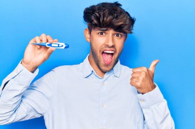 Termometreyi tutan İspanyol genç adam parmağıyla yan tarafa bakıyor. Ağzını açarak gülümsüyor. 