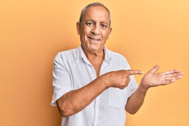 Yakışıklı, beyaz tişört giyen olgun bir adam kameraya hayret ediyor ve gülümsüyor. Elinle gösterip parmağınla işaret ediyor.. 