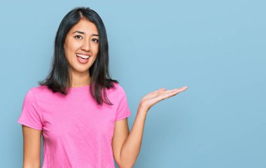 Güzel Asyalı genç bir kadın, günlük pembe tişört giyiyor, gülümsüyor, eli avucunda kameraya bakıyor ve gülümsüyor.. 
