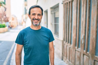 Orta yaşlı, sakallı, açık havada mutlu gülümseyen bir adam.