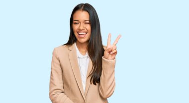 Güzel İspanyol kadın, iş ceketi giyiyor, gülümsüyor, kameraya göz kırpıyor zafer işareti yapıyor. İki numara.. 