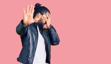 Genç Arap adam, sıradan deri ceket giyiyor, elleriyle gözleri örtüyor ve üzgün ve korku ifadeleriyle jest yapıyor. utangaç ve olumsuz kavram. 