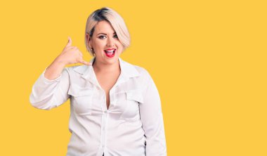 Sarışın, iri yarı, rahat tişört giyen, gülümseyen, el ve parmaklarıyla telefon hareketi yapan, telefonda konuşan bir kadın. iletişim kavramları. 