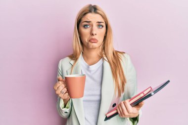 Kafkasyalı genç bir kadın bir fincan kahve içiyor ve elinde dizüstü bilgisayar var. Depresyonda ve endişe içinde, sinirli ve korkmuş bir halde. hüzünlü ifade. 