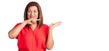 Orta yaşlı Latin kadın gündelik giysiler giyip kameraya hayret ediyor ve gülümsüyor.. 