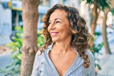 Orta yaşlı İspanyol kadın gülümseyerek şehirde mutlu mesut yürüyor..