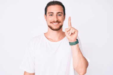 Gündelik beyaz tişört giyen genç yakışıklı bir numaralı parmağını gösterip onu gösterirken kendinden emin ve mutlu bir şekilde gülümsüyor.. 