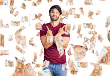 Her iki tarafı parmaklarıyla gösteren günlük kıyafetler giyen yakışıklı İspanyol adam farklı yönlere bakıyor.