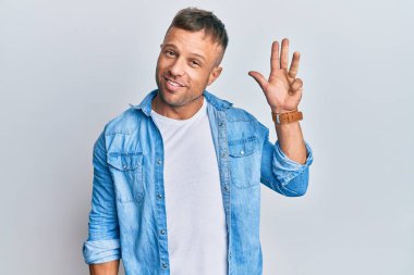 Yakışıklı, sıradan kot ceket giyen kaslı adam dört numarayı gösterip işaret ederken kendine güvenen ve mutlu bir şekilde gülümsüyor.. 