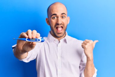 Termometreyi tutan genç, yakışıklı kel adam baş parmağını yana kaldırıyor ve ağzı açık gülümsüyor. 