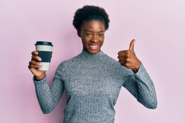 Genç Afro-Amerikan kızı kahveyi alıp götürüyor mutlu ve olumlu gülümsüyor, başparmağını kaldırıyor ve onaylıyor. 