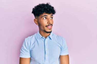 Genç Arap yakışıklı adam günlük giysiler giyiyor, rahat bir görünüm takınıyor, doğal bir yüz ve kendine güvenen bir gülümsemeyle poz veriyor.. 