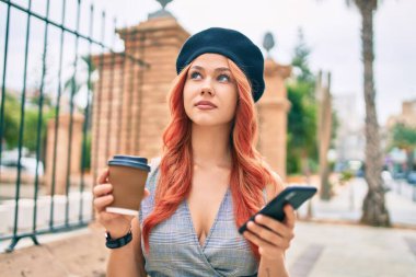 Genç kızıl saçlı kız. Akıllı telefon kullanmak ve şehirde kahve içmek ciddi bir ifade..
