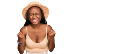 Genç siyah kadın, yaz şapkası takıyor. Çok mutlu ve heyecanlı. Kolları havada, gülümseyen ve başarı için bağıran kazanan bir jest yapıyor. kutlama konsepti. 