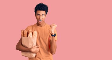 Genç Afro-Amerikalı adam elinde kağıt torbayla kızgın ve kızgın bir şekilde yumruğunu kaldırıyor ve öfkeyle bağırıyor. öfke ve agresif konsept. 