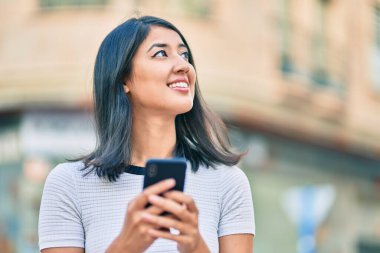 Genç İspanyol kadın şehirde akıllı telefon kullanarak mutlu bir şekilde gülümsüyor..