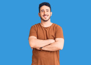 Gündelik kıyafetler giyen, kollarını kavuşturup kameraya gülümseyen genç İspanyol adam. pozitif kişi. 