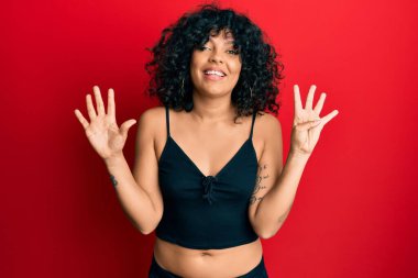 Kolsuz tişörtlü, gündelik giyinen genç İspanyol kadın dokuz numarayı gösteriyor ve gülümsüyor. Kendinden emin ve mutlu.. 