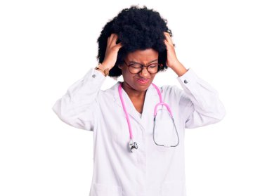 Genç Afro-Amerikalı kadın doktor önlüğü ve steteskop giyiyor. Ağrı ve migren yüzünden çaresiz ve stresli baş ağrısı çekiyor. Eller başının üstünde.. 