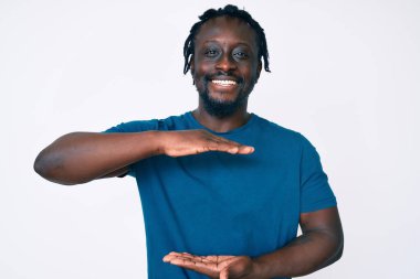 Saçları örgülü, el kol hareketleri yapan, büyük boy ve ölçü işareti olan Afro-Amerikan genç bir adam. Kameraya bakıp gülümsüyor. ölçüm kavramı. 