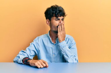 Gündelik giysiler giyen genç İspanyol adam masada oturup ağzını eliyle kapatmaktan sıkılmış. Huzursuz ve uykulu.. 