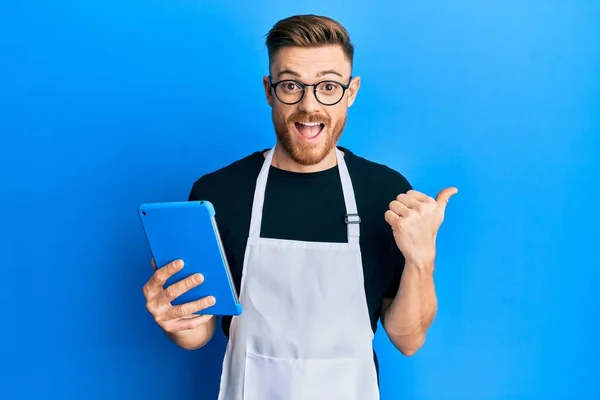 Jovem Ruiva Vestindo Avental Profissional Usando Touchpad Apontando Polegar Até — Fotografia de Stock