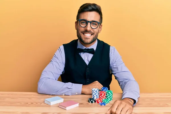 英俊而惊慌失措的男人坐在桌子上 拿着扑克牌和卡片 面带微笑 面带微笑 面带微笑 显得积极而快乐 — 图库照片
