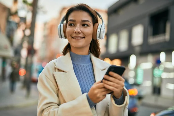 街中でスマホやヘッドフォンを使って笑顔で幸せそうな若いヒスパニック系女性 — ストック写真