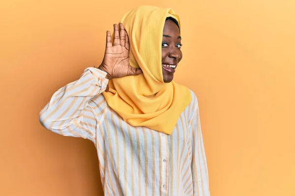 Beautiful african young woman wearing traditional islamic hijab scarf smiling with hand over ear listening an hearing to rumor or gossip. deafness concept.