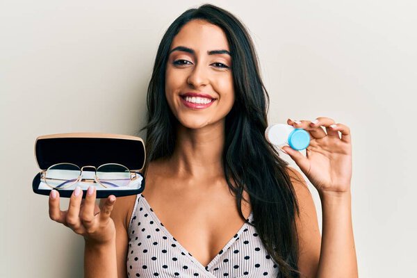 Красивая латиноамериканка, держащая очки и контактные линзы, улыбается счастливой и прохладной улыбкой на лице. показывая зубы. 