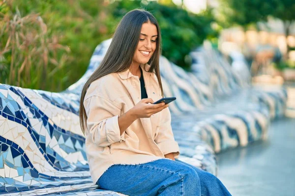 若いですヒスパニック系の女の子笑顔幸せな使用してスマートフォンで公園 — ストック写真