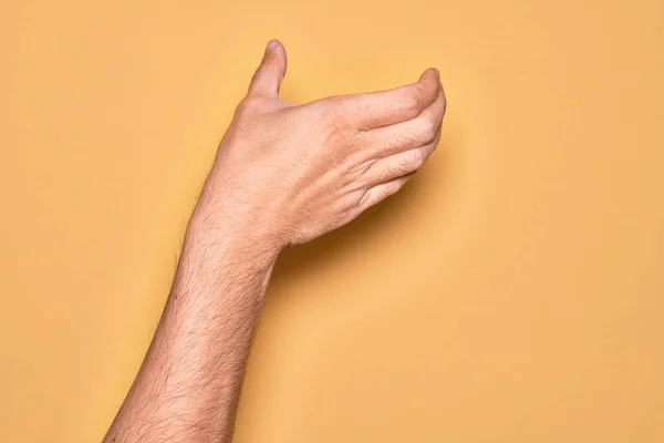白人年轻人的手 手拿着看不见的东西 用手指捂住孤立的黄色背景 空空的手做剪断和抓取动作 — 图库照片