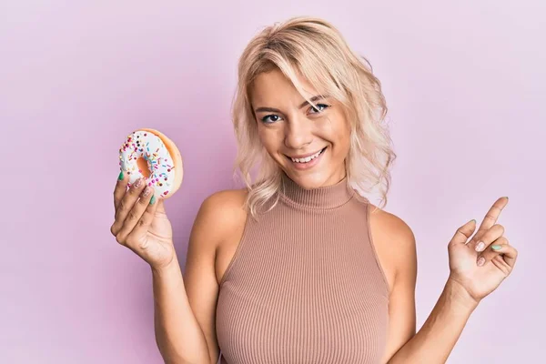 Joven Chica Rubia Sosteniendo Donut Sonriendo Feliz Señalando Con Mano —  Fotos de Stock