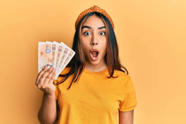 Young Latin Woman Holding United Kingdom Pounds Banknotes Scared Amazed — Stok fotoğraf