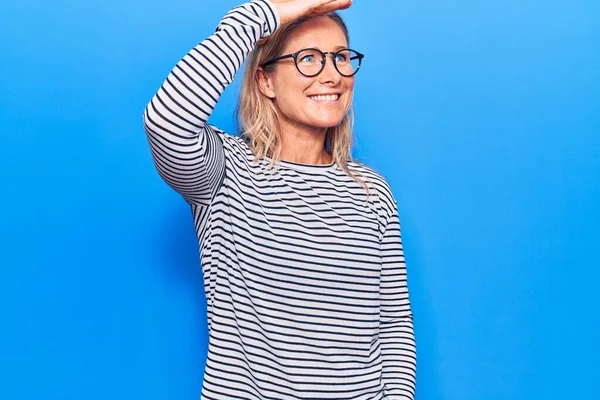 중년의 여성은 줄무늬 스웨터를 안경을 바라보며 미소짓는다 — 스톡 사진