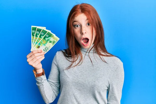 Genç kızıl saçlı kız 50 İsrail şekeri tutuyor. Banknotlar korkmuş ve ağzı açık kalmış, şaşırmış, inançsız bir yüz. 