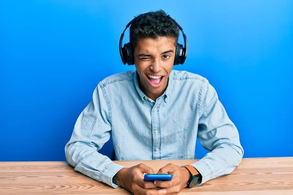 Joven Hombre Afroamericano Guapo Usando Teléfono Inteligente Con Auriculares Guiñando —  Fotos de Stock