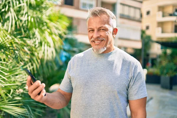 在公园里用智能手机快乐地微笑着的中年惊慌失措的白发男人 — 图库照片