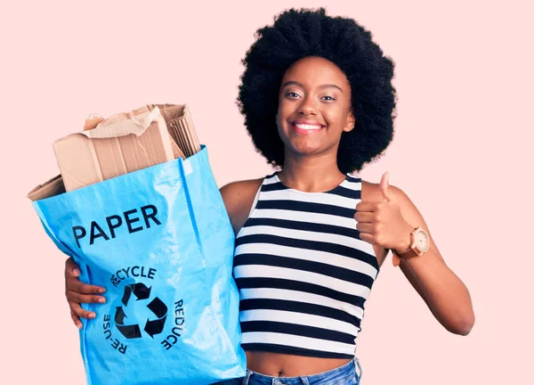 紙と段ボールの笑顔でリサイクルバッグを保持若いアフリカ系アメリカ人女性幸せと肯定的な 親指を行う優れた承認サイン — ストック写真