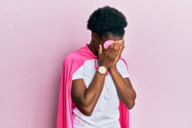 Genç Afro-Amerikalı kız süper kahraman maskesi ve pelerin giyip ağlarken suratını ellerle kapatan üzgün bir ifade takınıyor. depresyon kavramı. 