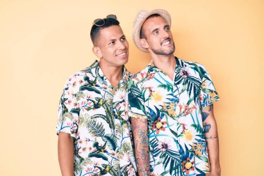 Yazlık şapkalı ve Hawaii tişörtlü iki genç eşcinsel yüzünde gülümseme, doğal bir ifade ile yan yana bakıyorlar. Kendinden emin gülen. 