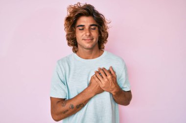 Gündelik kıyafetler giyen genç İspanyol adam elleri göğsünde, gözleri kapalı ve yüzünde minnet dolu bir jest ile gülümsüyor. sağlık kavramı. 