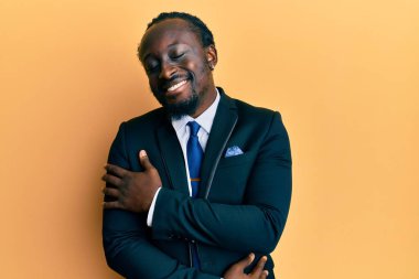 Yakışıklı, takım elbiseli ve kravatlı genç bir adam mutlu ve pozitif, kendinden emin bir şekilde kendine sarılıyor. Sevgi ve özgüven. 