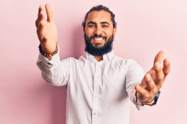 Gündelik giysiler giymiş genç bir Arap, kameraya sarılmak için kollarını açmış gülümseyerek bakıyor. Mutluluğu kucaklayan neşeli bir ifade.. 